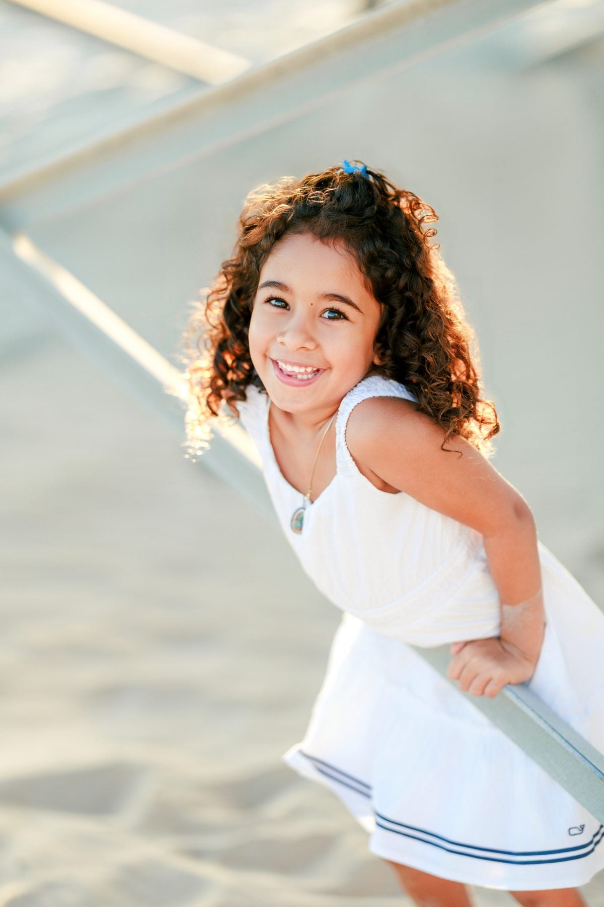 Curly-haired girl grins while leaning on railing above the beach