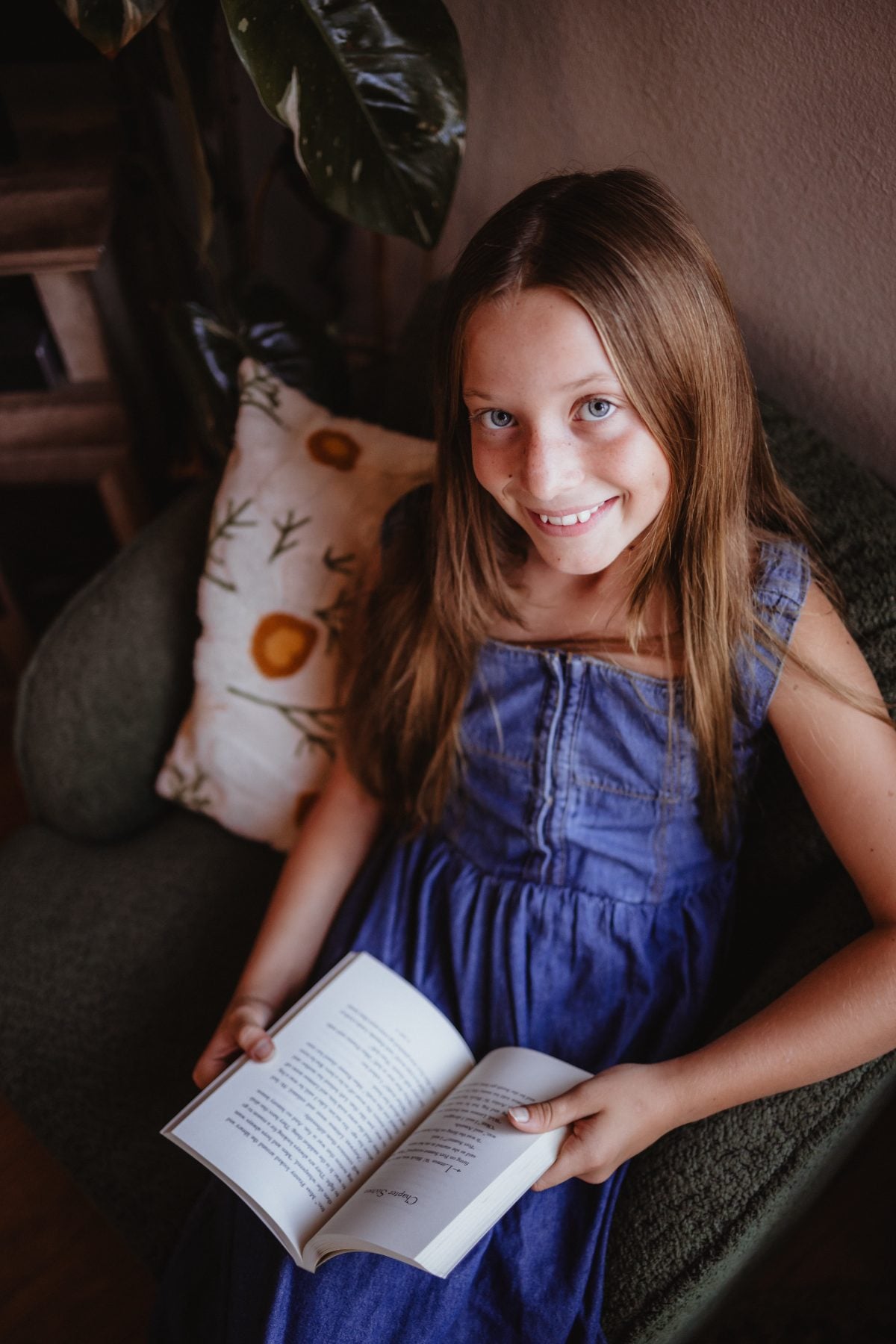 Girl in blue dress smiling at camera while holding open book