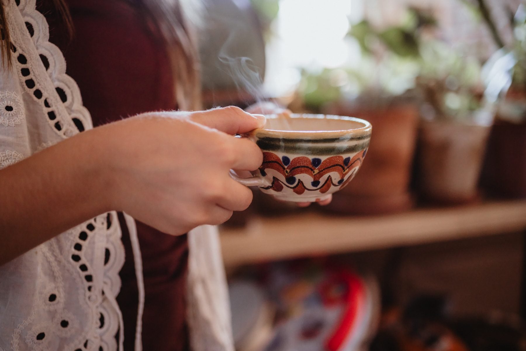 Woman holds steaming ceramic mug near potted plants in Lakeside, California home