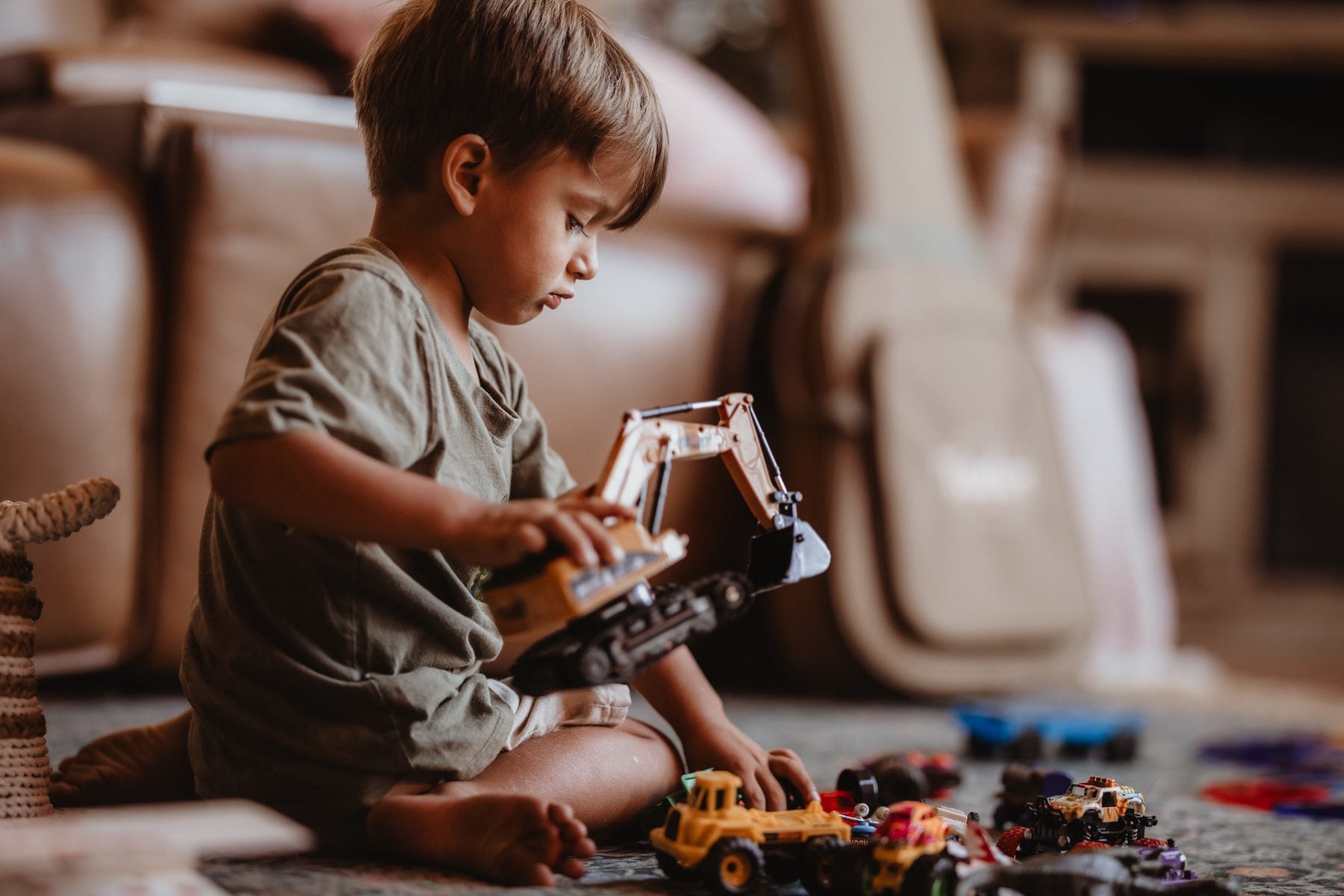 Toddler boy plays intently with a toy excavator on the carpet