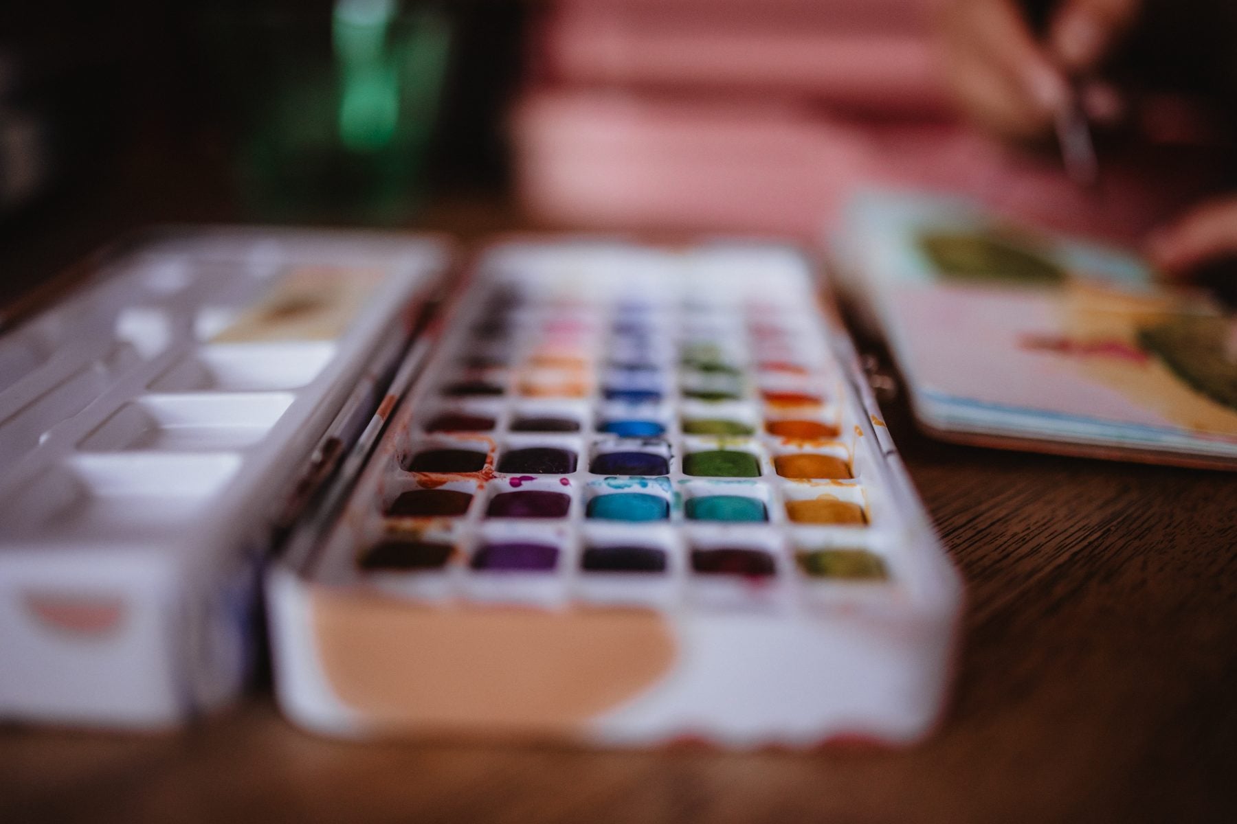 Close-up of an open watercolor paint palette on a wooden desk