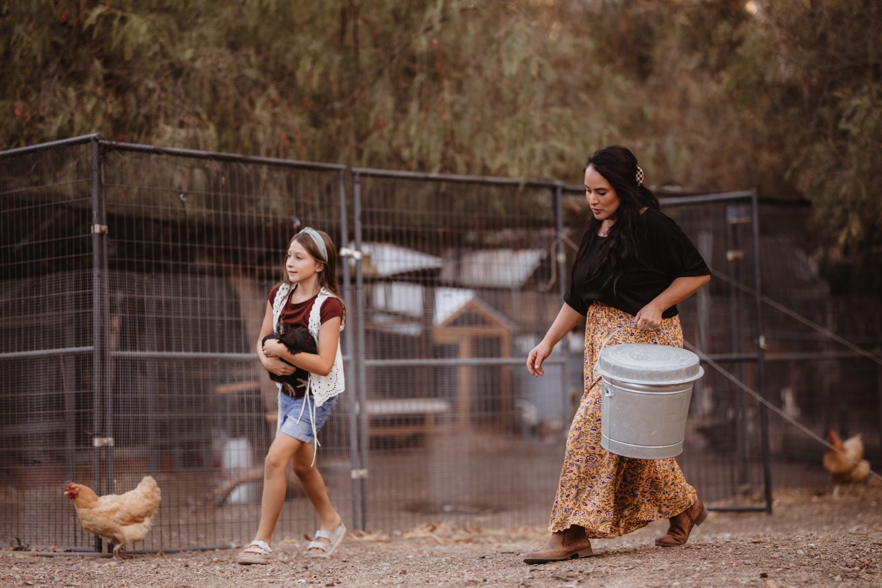 Woman and girl walk past chicken coop carrying a bucket
