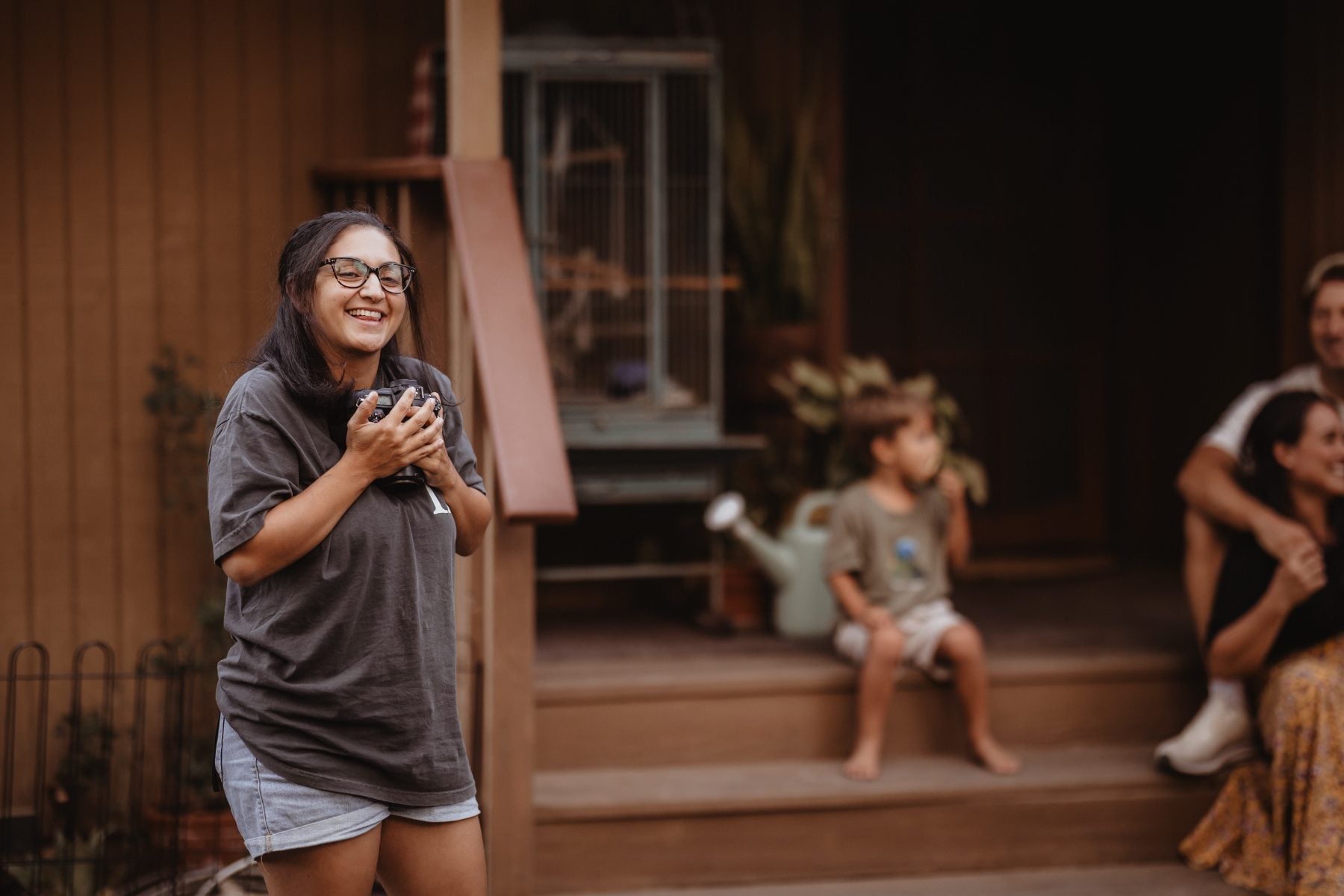 Woman laughing holds a chicken on porch as family watches nearby