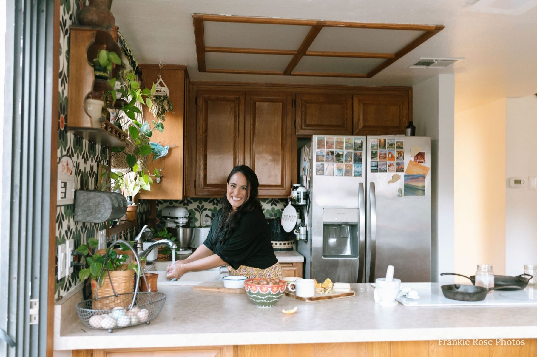 Woman washes fresh produce at kitchen counter surrounded by houseplants