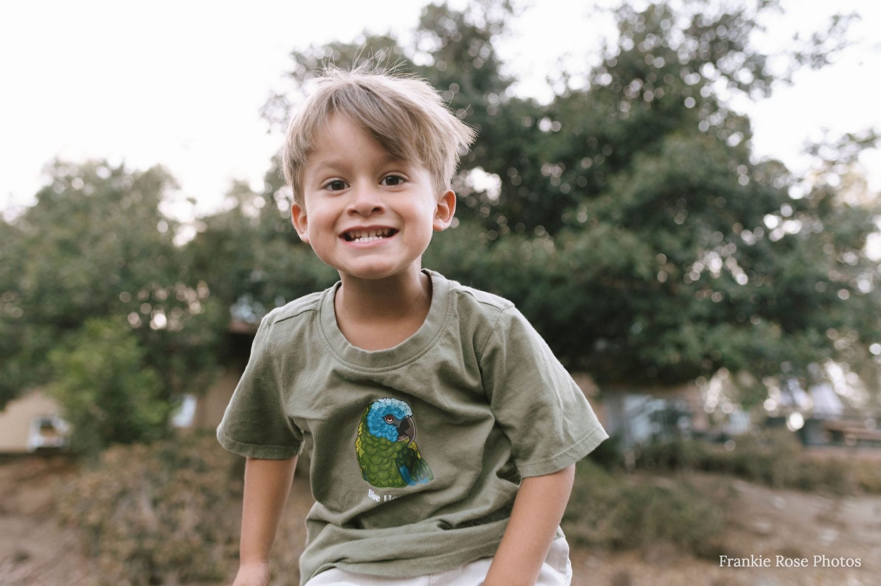 Young boy in green shirt smiles outdoors in Lakeside backyard